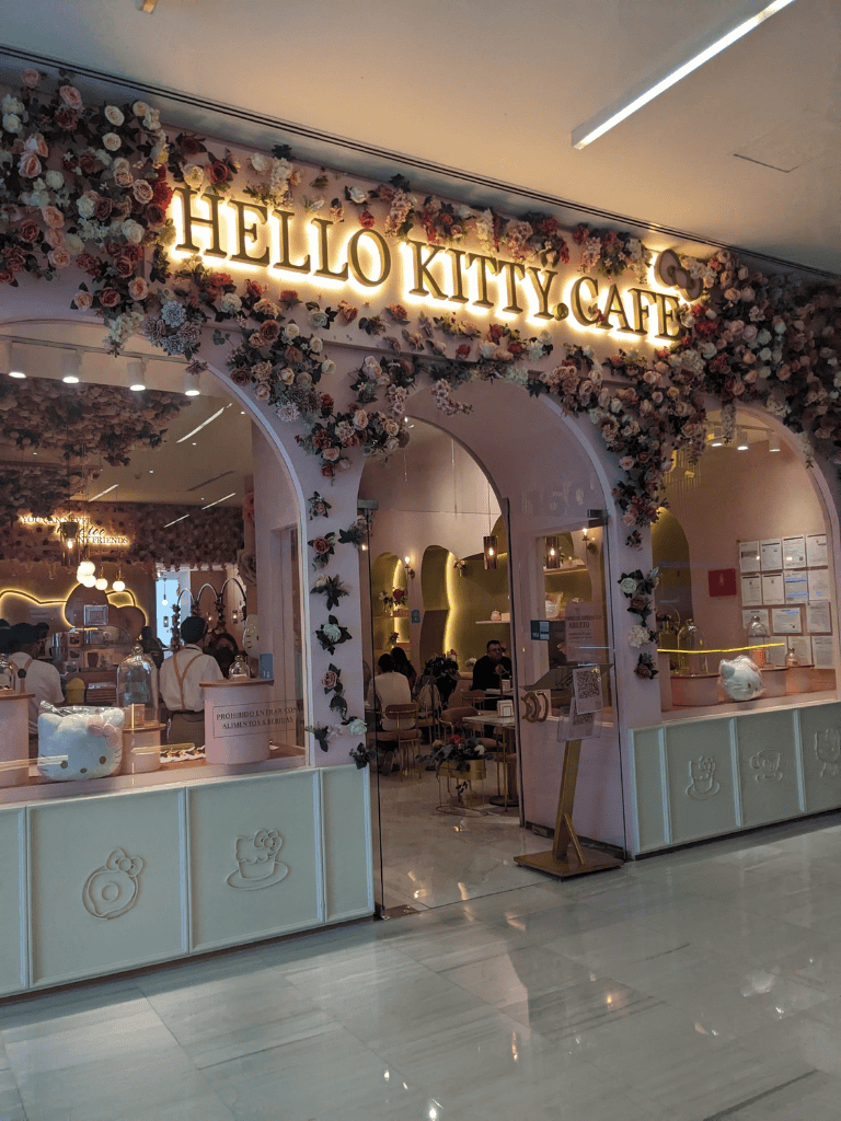 Hello Kitty Cafe entrance decorated with pink flowers, inviting fans of Hello Kitty and cute cafes.