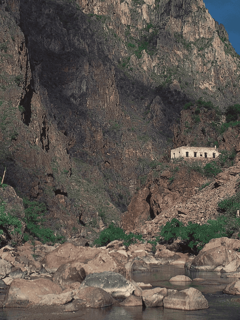 Ancient building on rocky mountain landscape with river in foreground, rugged terrain, QuestForDirections.
