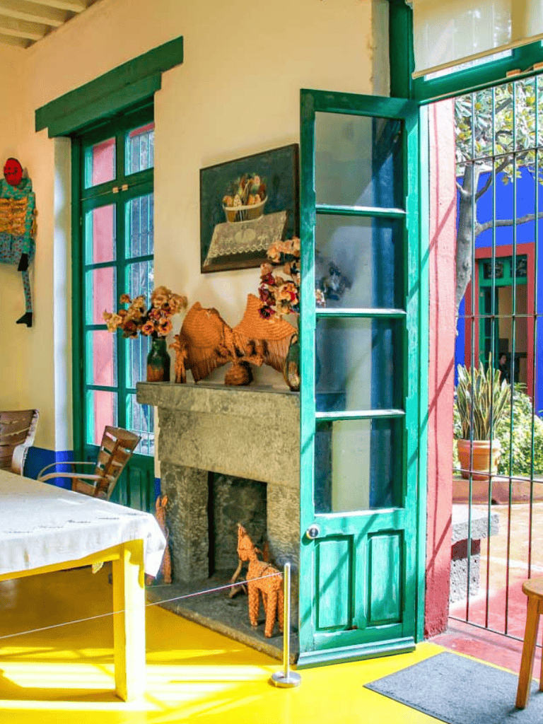 Colorful interior of a cozy, rustic cafe with decorated mantle, vibrant flowers, and bright green window and door frames.