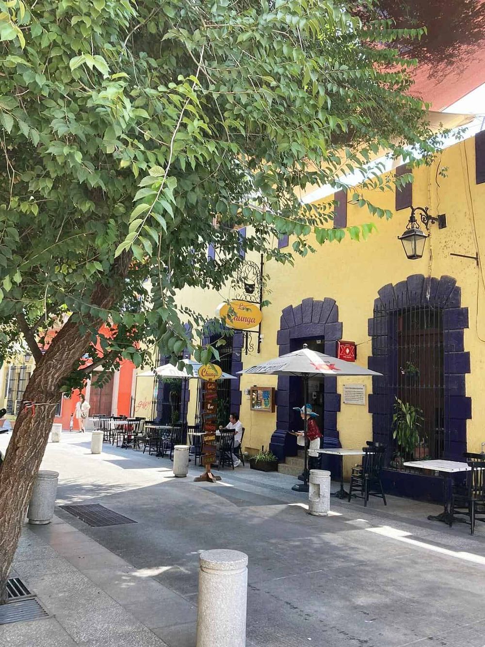Colorful Mexican street café with outdoor seating and lush greenery, perfect for dining and relaxation.