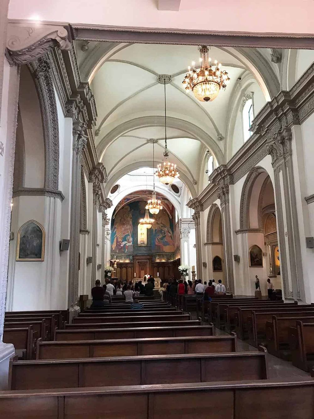 Intricate church interior with high vaulted ceilings and elegant chandeliers, showcasing historic architecture and religious art.