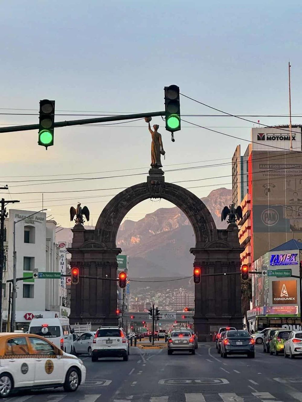 Historic monument at the intersection in Mexico City with traffic lights and cityscape background.