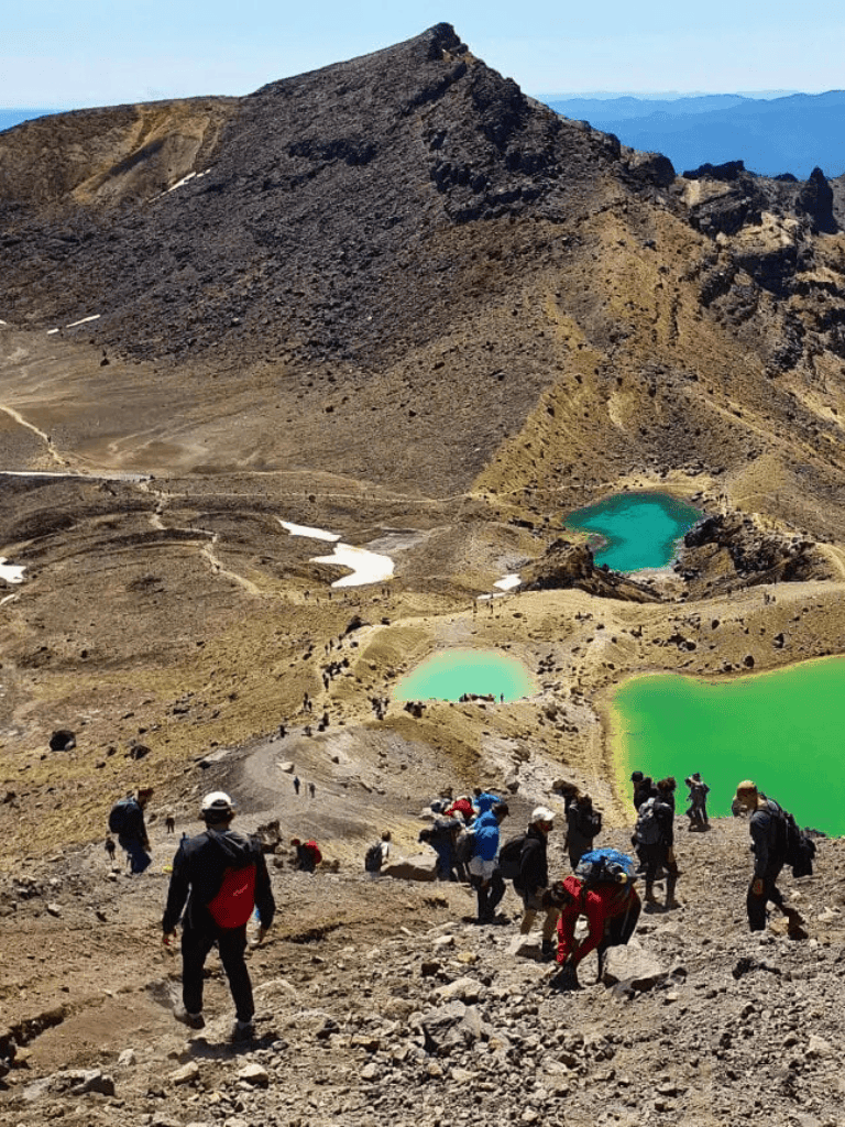 Vibrant green crater lakes on volcanic mountain with hikers trekking on rugged terrain.
