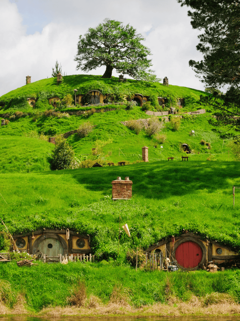 Cozy Hobbit holes nestled in lush green hills with a large tree at the top, inspired by the Lord of the Rings.