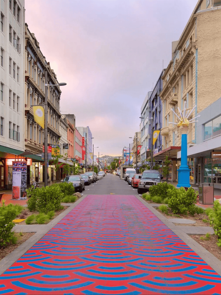 Vibrant city street with colorful buildings, shopping, and a patterned crosswalk during sunset.