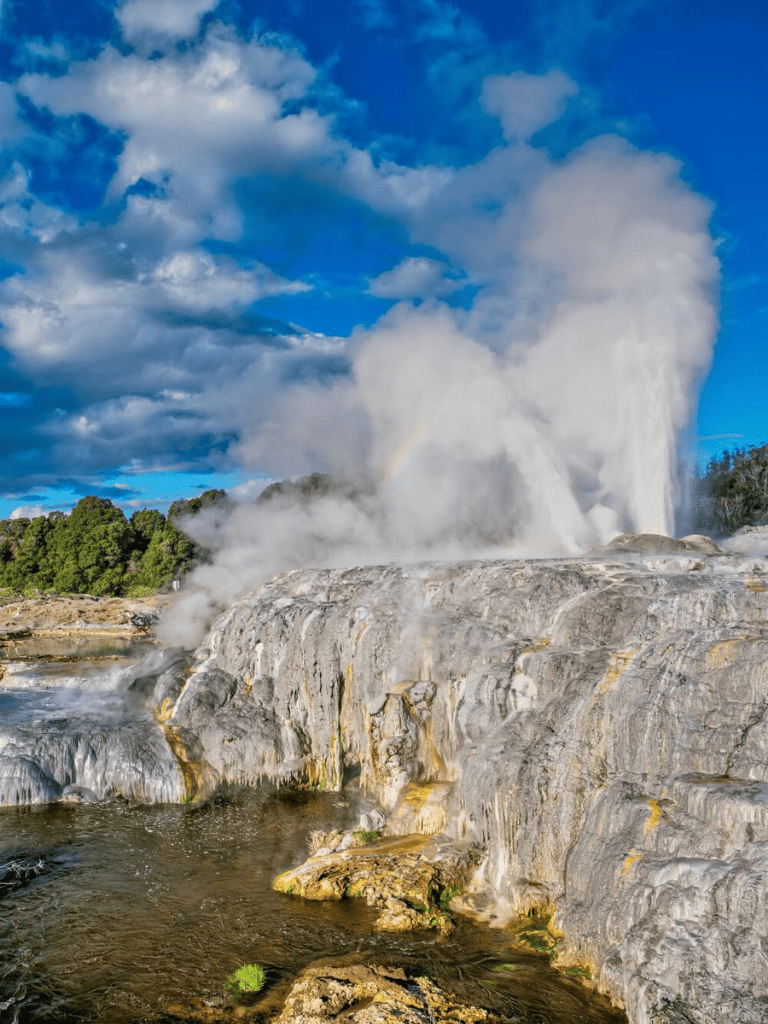 Steam erupting from geothermal hot springs against a blue sky with clouds.