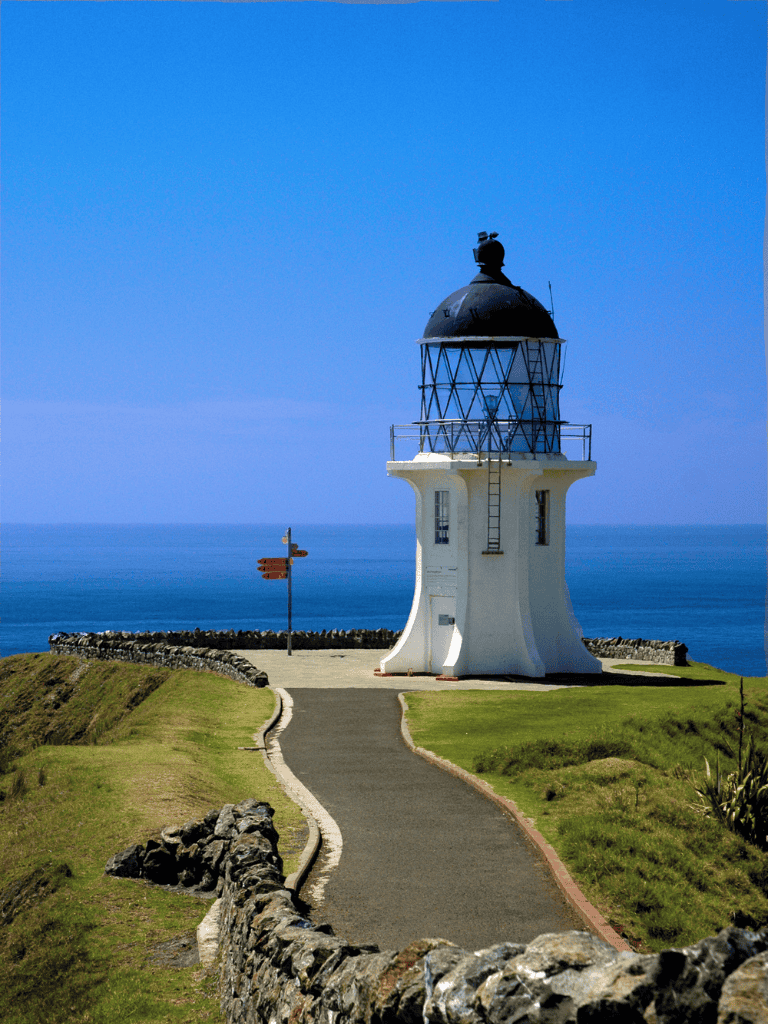 Lighthouse on coastal landscape with blue sky and ocean, guiding travelers along scenic routes.
