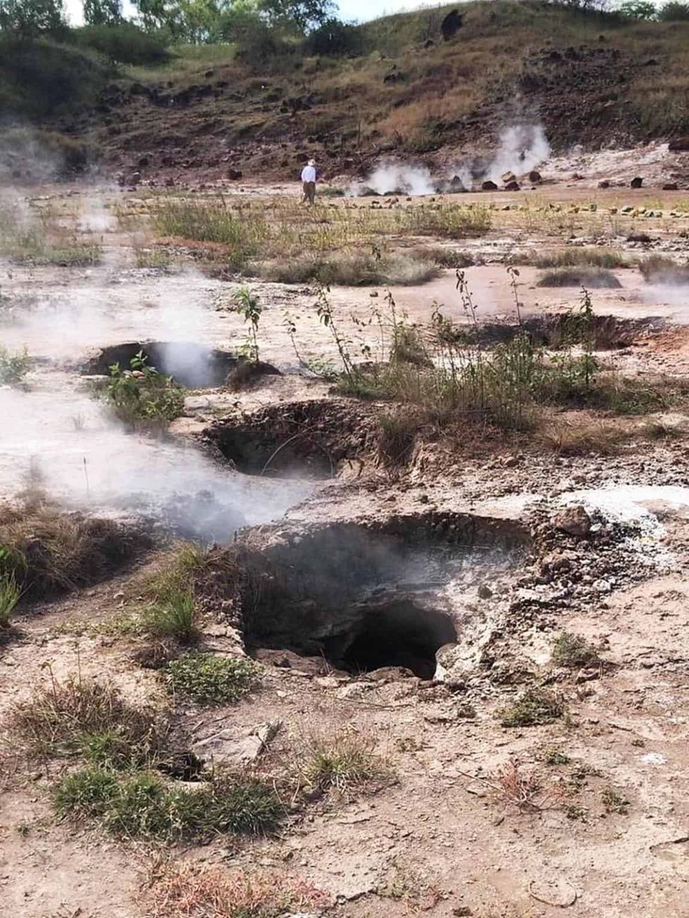 Steaming geothermal hot springs in a rugged outdoor landscape, with a person exploring near bubbling vents, highlighting adventure and natural wonders.