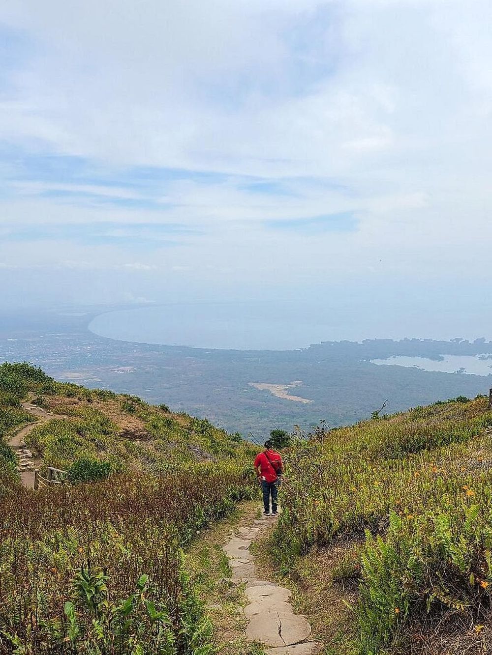 Scenic trail hike with ocean view, lush greenery, and cloudy sky, perfect for nature enthusiasts.