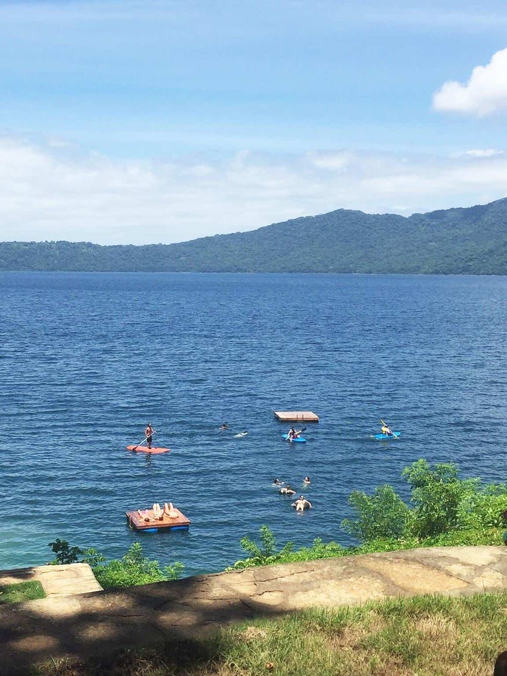 Kids playing on floating docks and paddleboarding on a scenic lake with surrounding mountains.