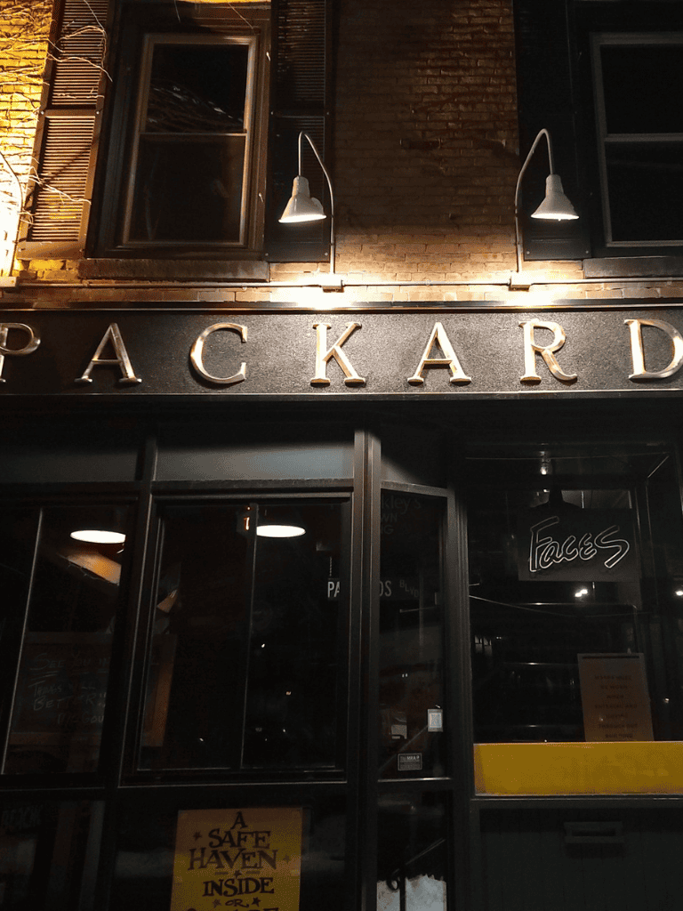 PACKARD sign exterior at night with illuminated building facade and vintage windows.