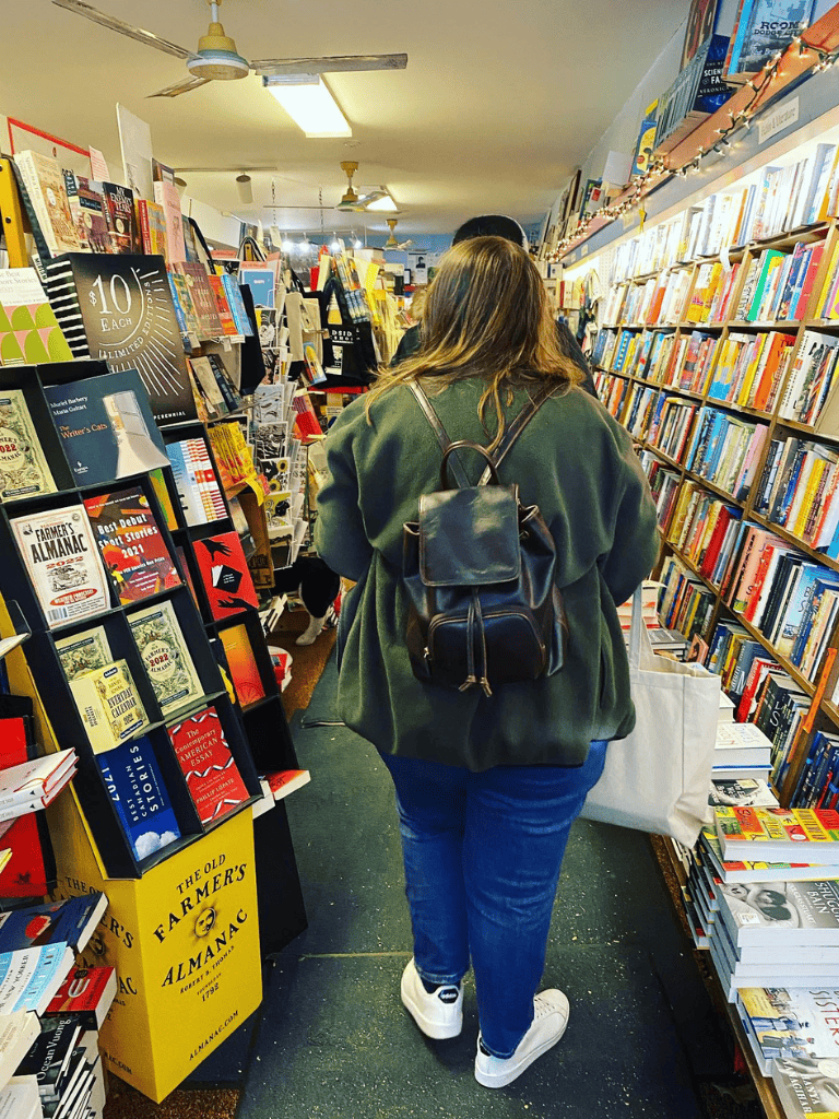 1. Woman browsing books in a bookstore aisle, focused on reading and shopping.