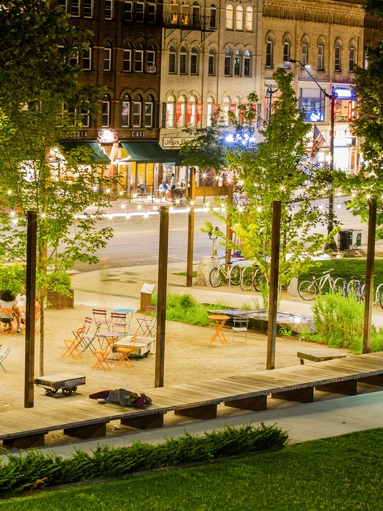 Outdoor city park at night with colorful seating and trees, illuminated by streetlights and urban buildings.