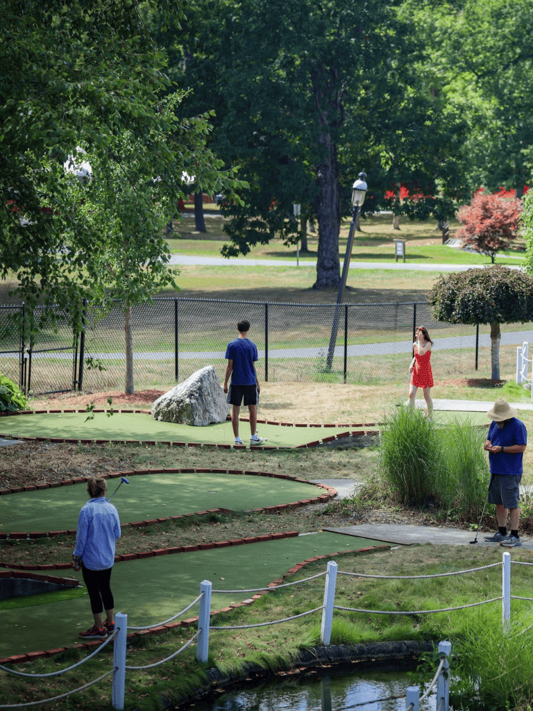 Miniature golf course with players enjoying a sunny day in a park setting.