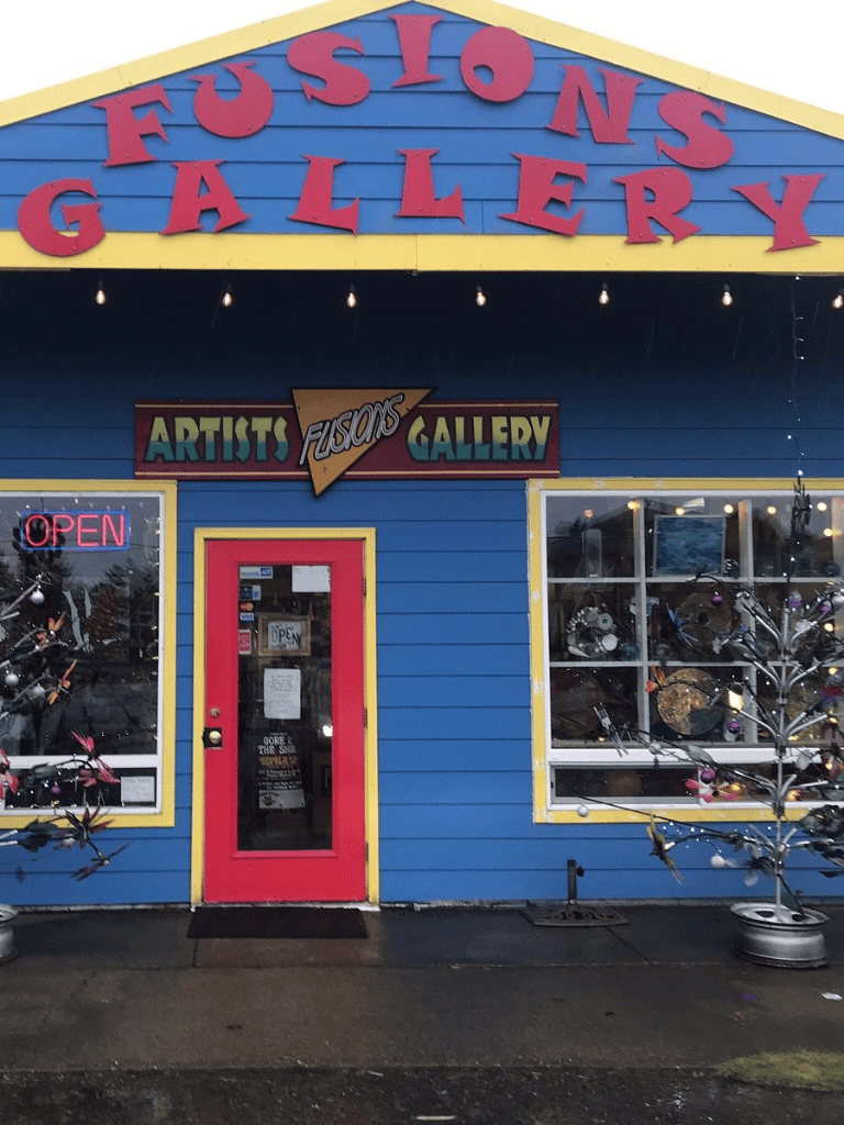 Colorful art gallery storefront with vibrant blue exterior and pink door, showcasing local artist artworks.