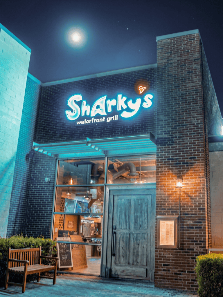 Sharky's waterfront grill restaurant at night with neon sign and outdoor seating.