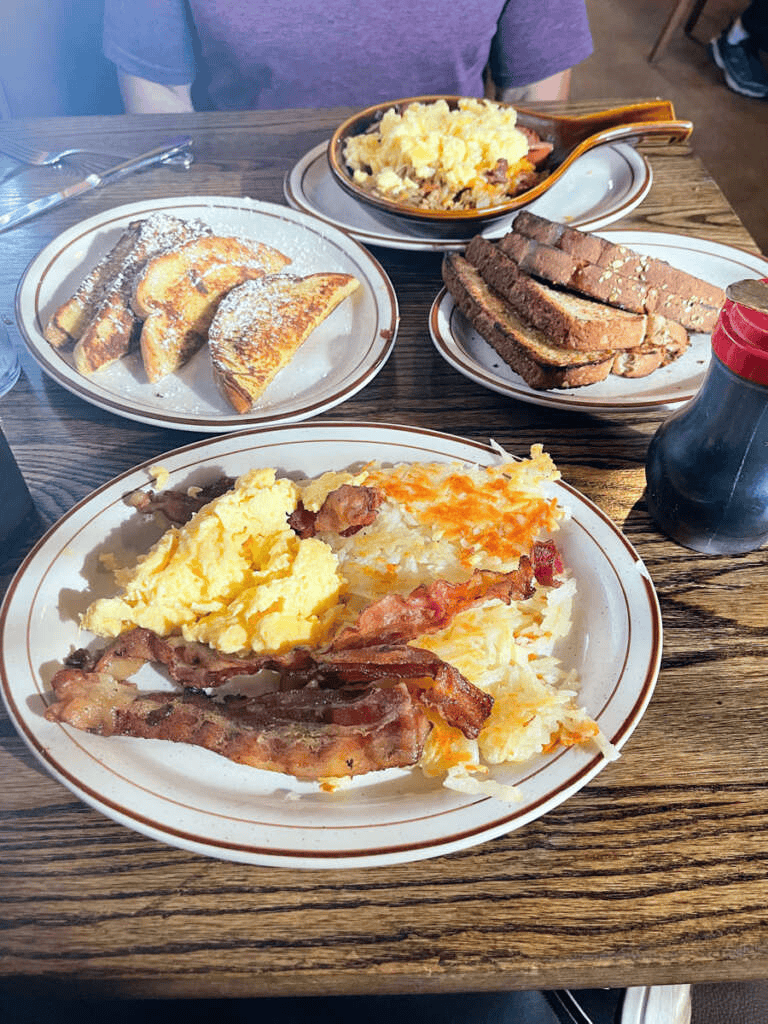 Savory breakfast with scrambled eggs, bacon, toast, French toast, and breakfast casserole on rustic wood table.