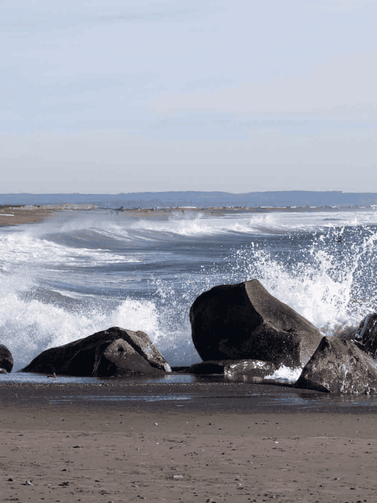 Vast ocean waves crashing against rocks on sandy beach, scenic coastal landscape, outdoor ocean adventure.