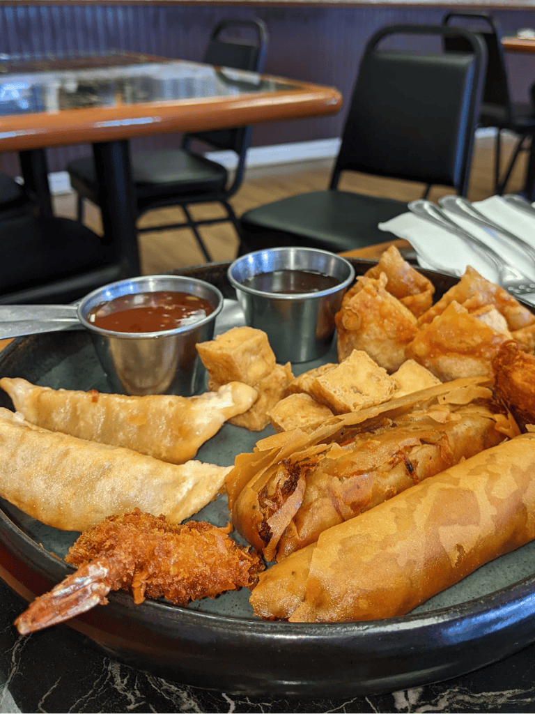 Crispy fried spring rolls, wontons, and tempura with dipping sauces on a restaurant table.