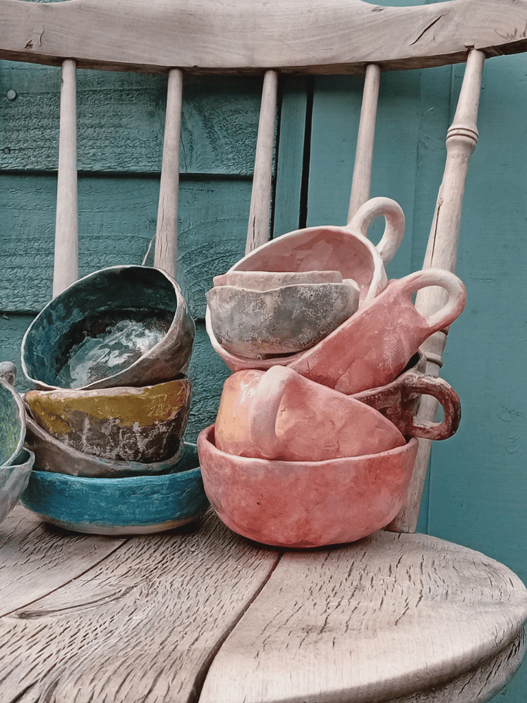 Clay pottery tea cups displayed on a rustic wooden chair, ideal for decor or collection.
