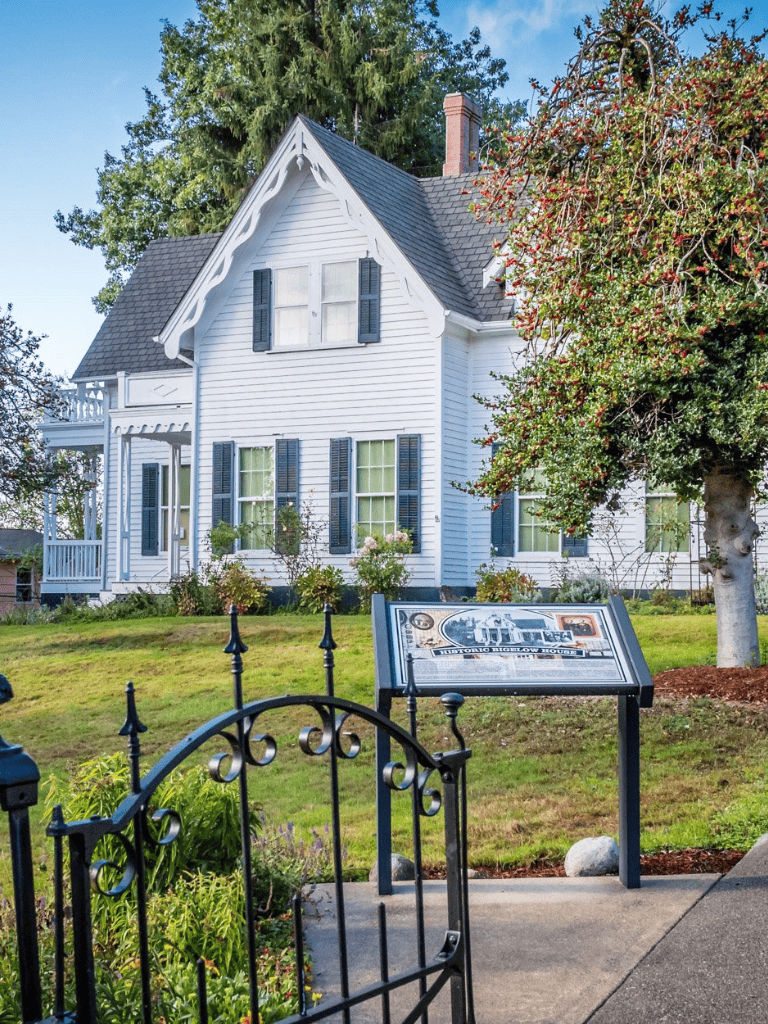 Charming historic white house with black shutters and welcoming garden, perfect for walking tours.