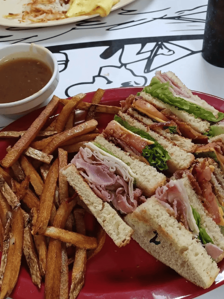 Crispy French fries with ham and turkey club sandwich on a red plate at a casual eatery.