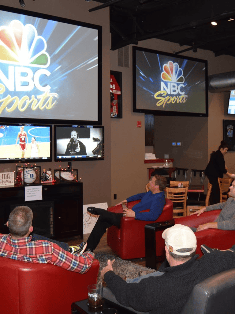 NBC Sports live sports broadcasting lounge with fans watching basketball and athletes' highlights.