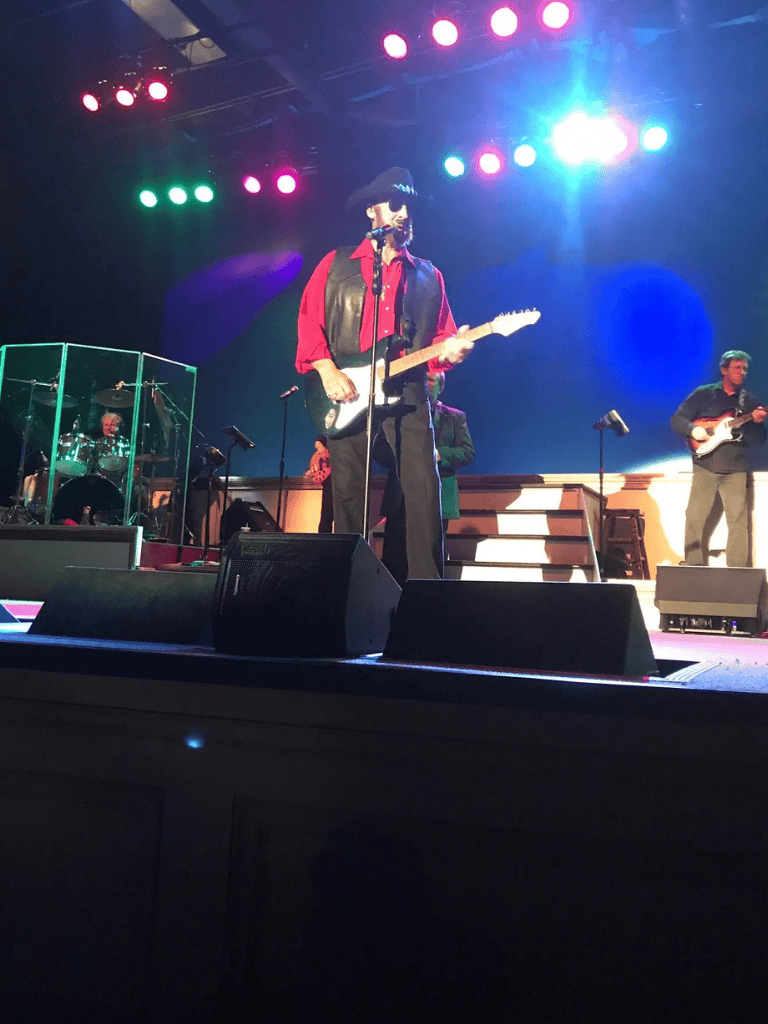 Vintage rock band performing live on stage with guitars and drums, colorful concert lighting, lively music atmosphere.