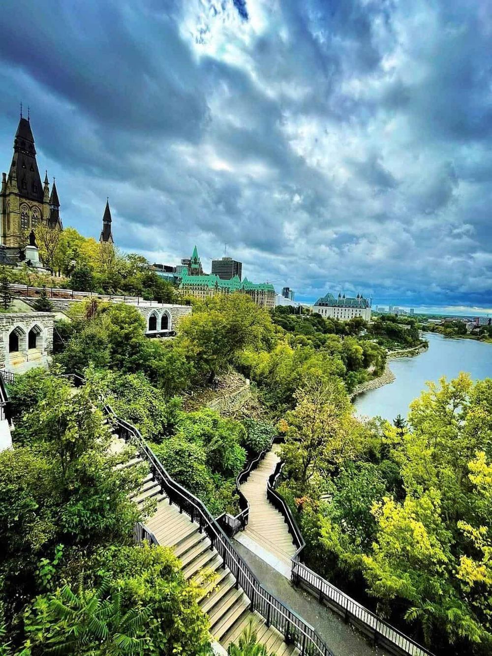 Scenic view of Ottawa River and Parliament Hill with lush greenery and vibrant city skyline in the background.