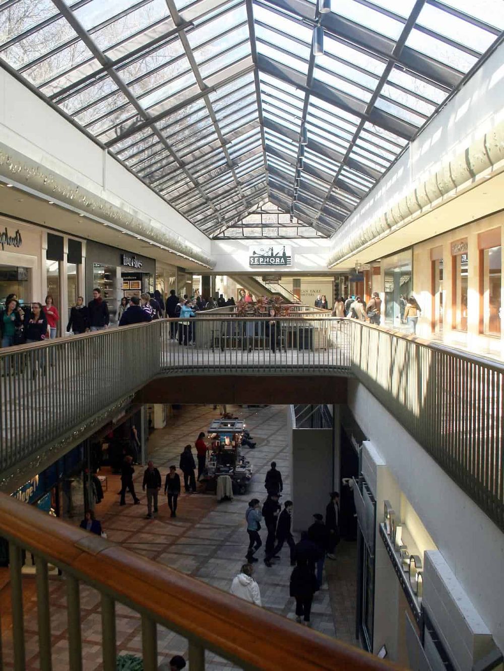 Busy indoor shopping mall with skylight ceiling and multiple retail stores, including Sephora.