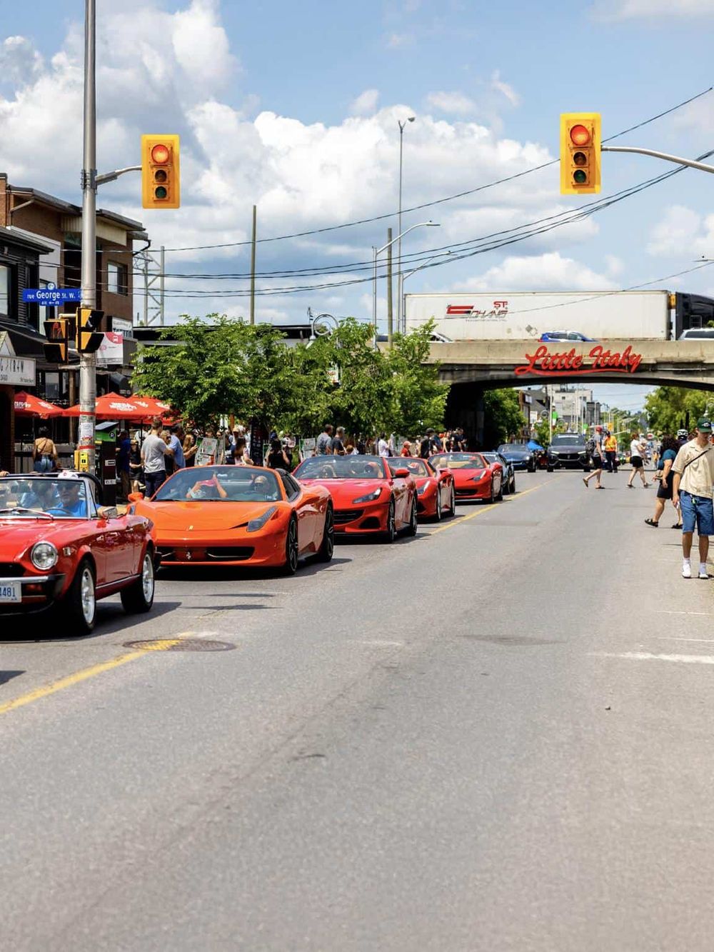 Luxury sports cars parked on a busy street in Little Italy, Toronto, with people walking and dining outside.