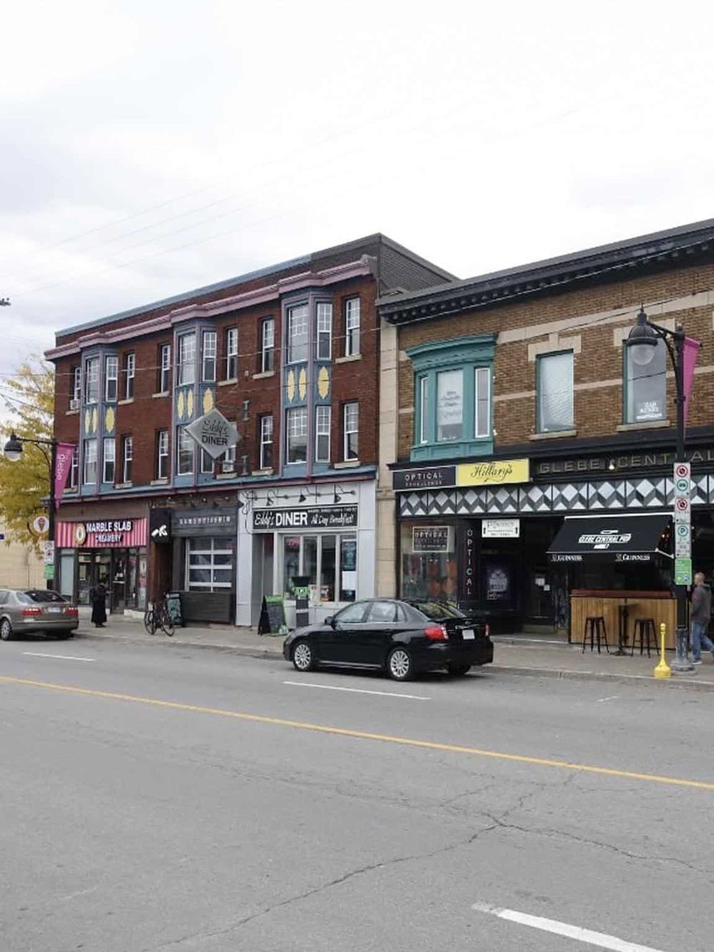 Colorful downtown storefronts with signage for local businesses and parked cars in a city street.