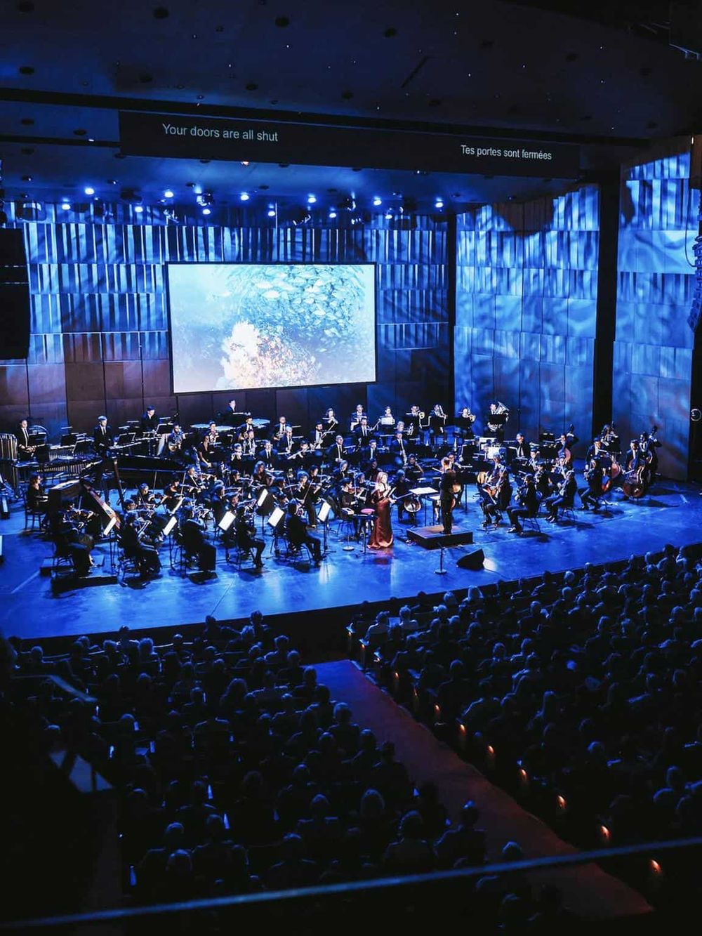Orchestral concert on stage with musicians and a conductor in a modern theater.