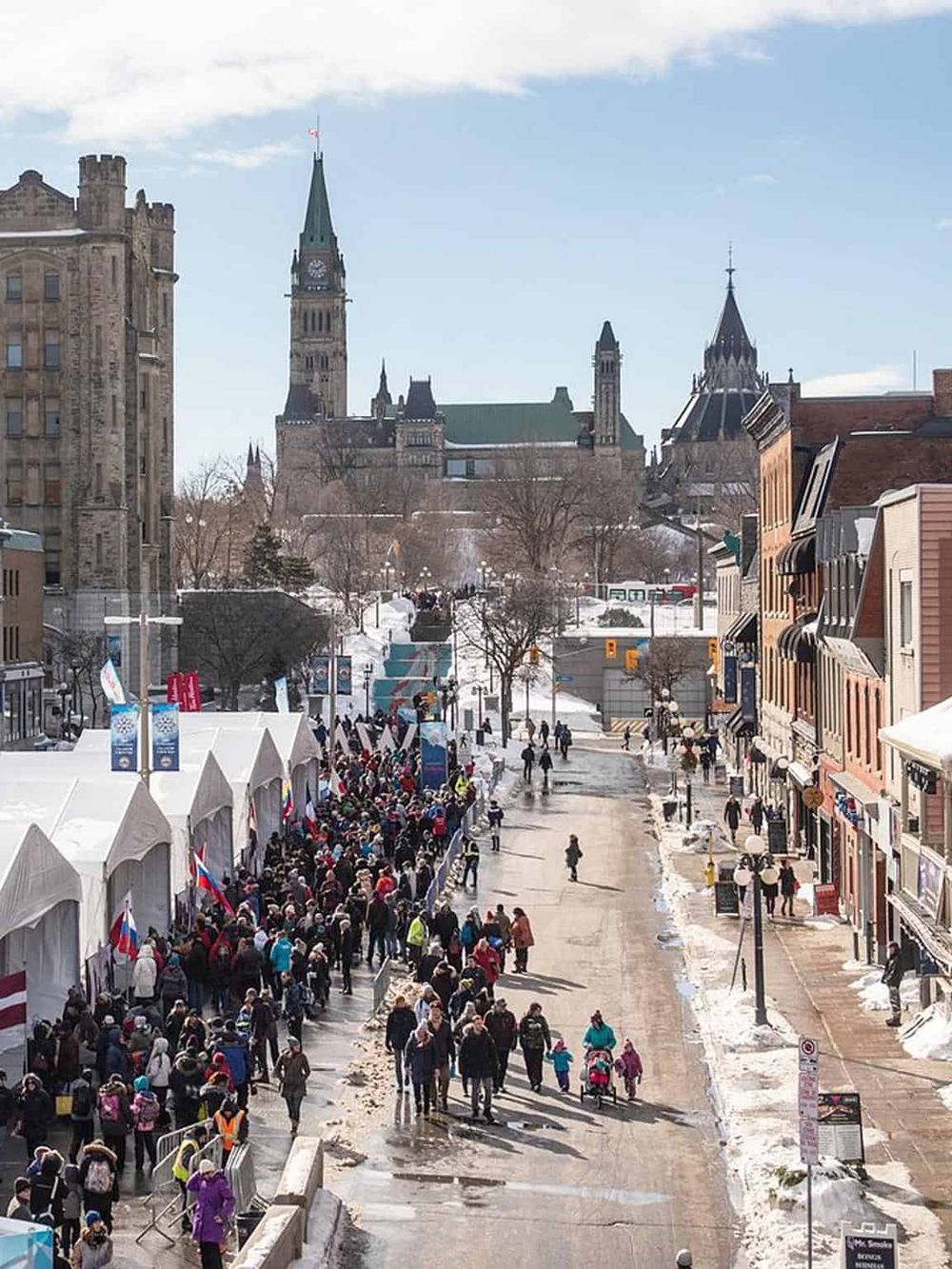Crowds gather along a snowy street with Parliament Hill in Ottawa, Canada, during winter festivities.