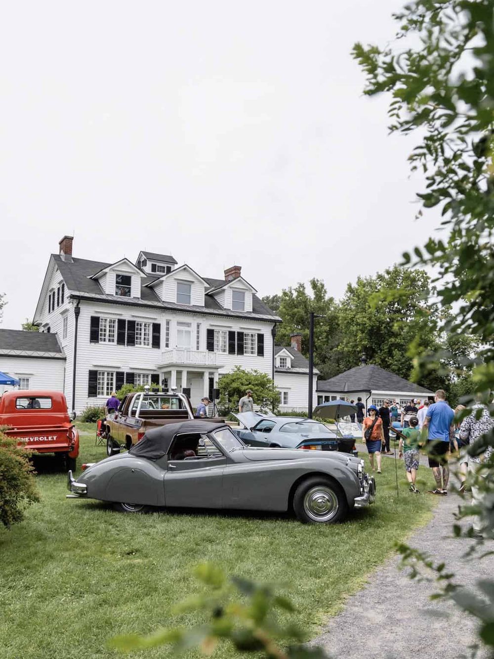 Classic car show outside a historic white mansion during a community event.