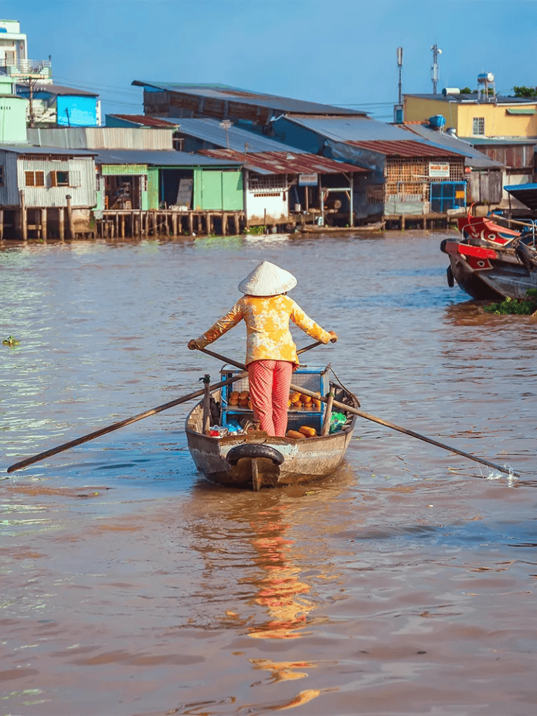 Traditional Vietnamese woman rowing boat along river at floating village, Vietnam.