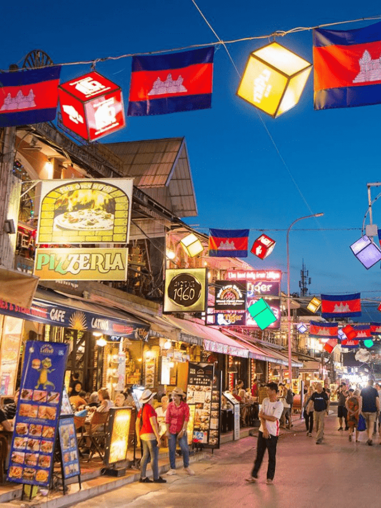 Colorful street scene with flags, neon signs, and restaurants at dusk in Phnom Penh, Cambodia.