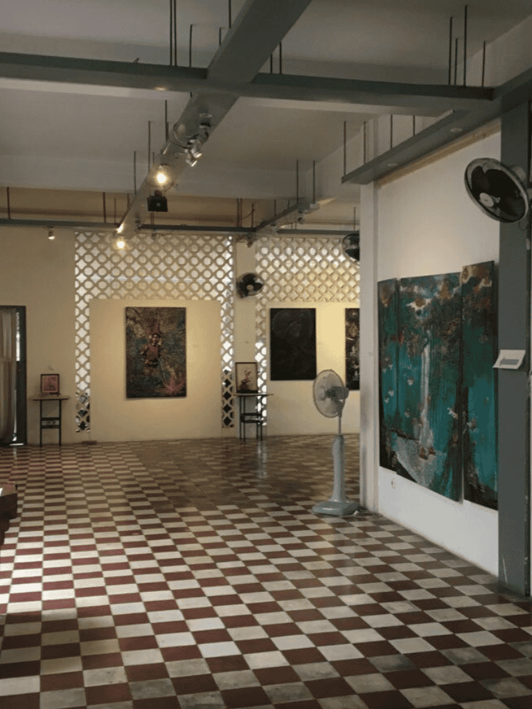 Elegant art gallery with paintings on white walls, checkered flooring, and ceiling fans, perfect for art enthusiasts.