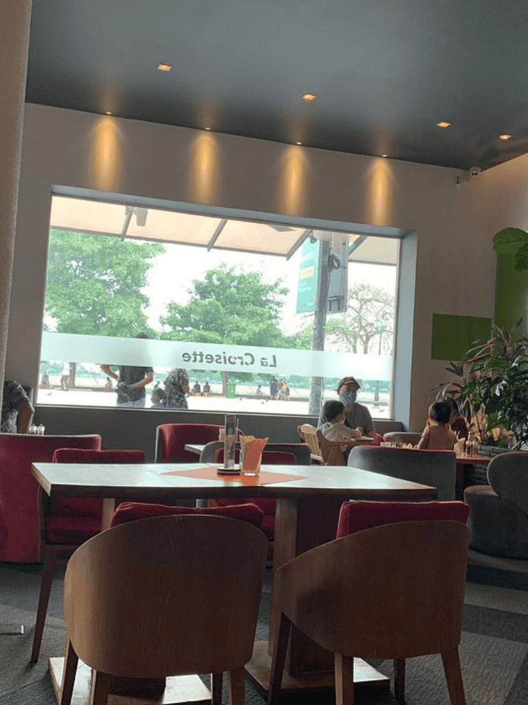 Quiet cafe interior with large window view and people dining, cozy ambiance for relaxation.