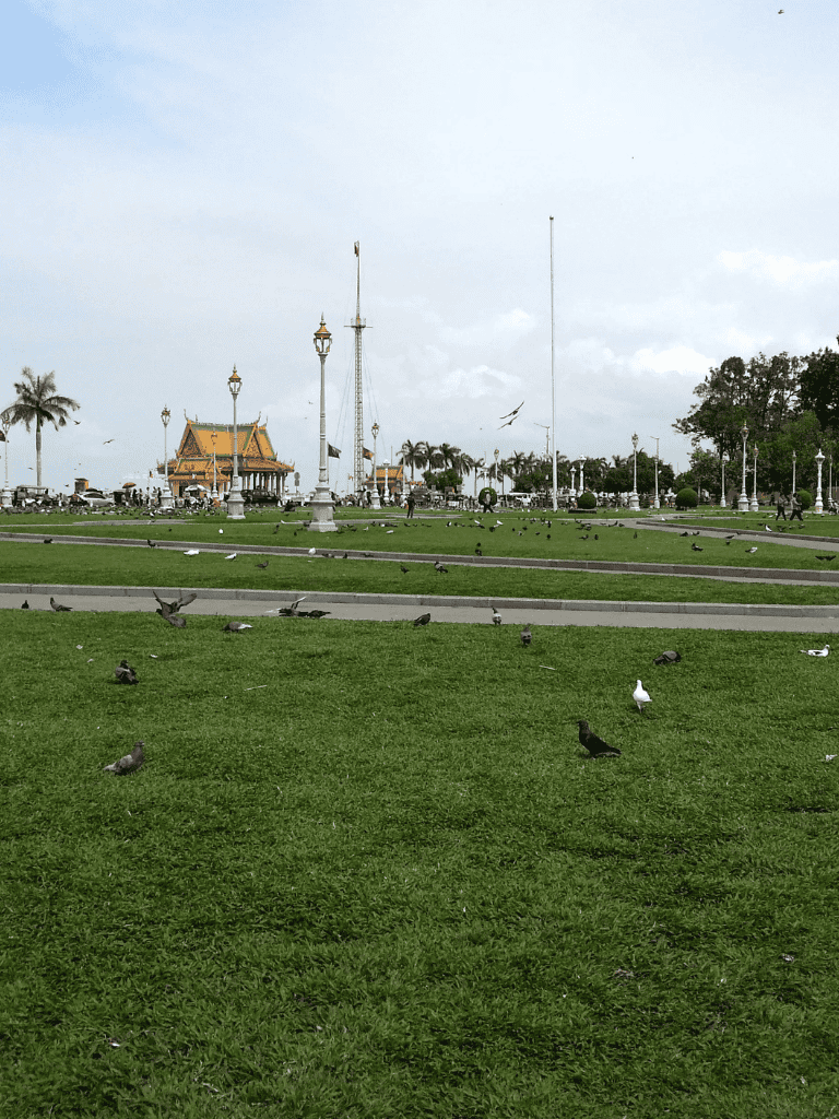Birds on lush green park lawn near traditional Thai temple in Bangkok, Thailand.