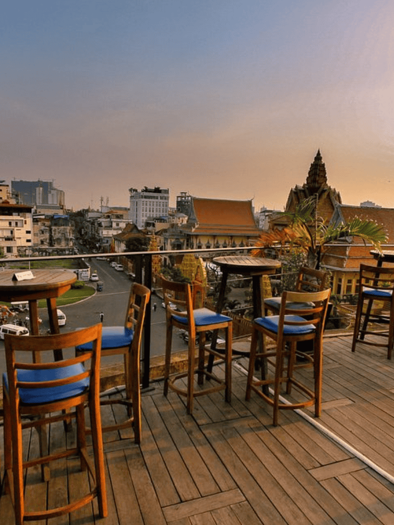 Vibrant cityscape view from a rooftop bar with outdoor seating and traditional architecture in the background.
