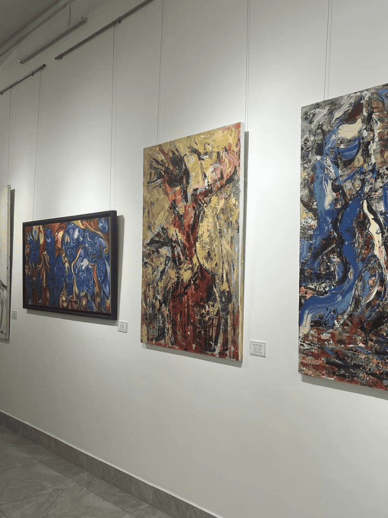 Vibrant abstract paintings display on a white gallery wall at QuestForDirections art exhibition.