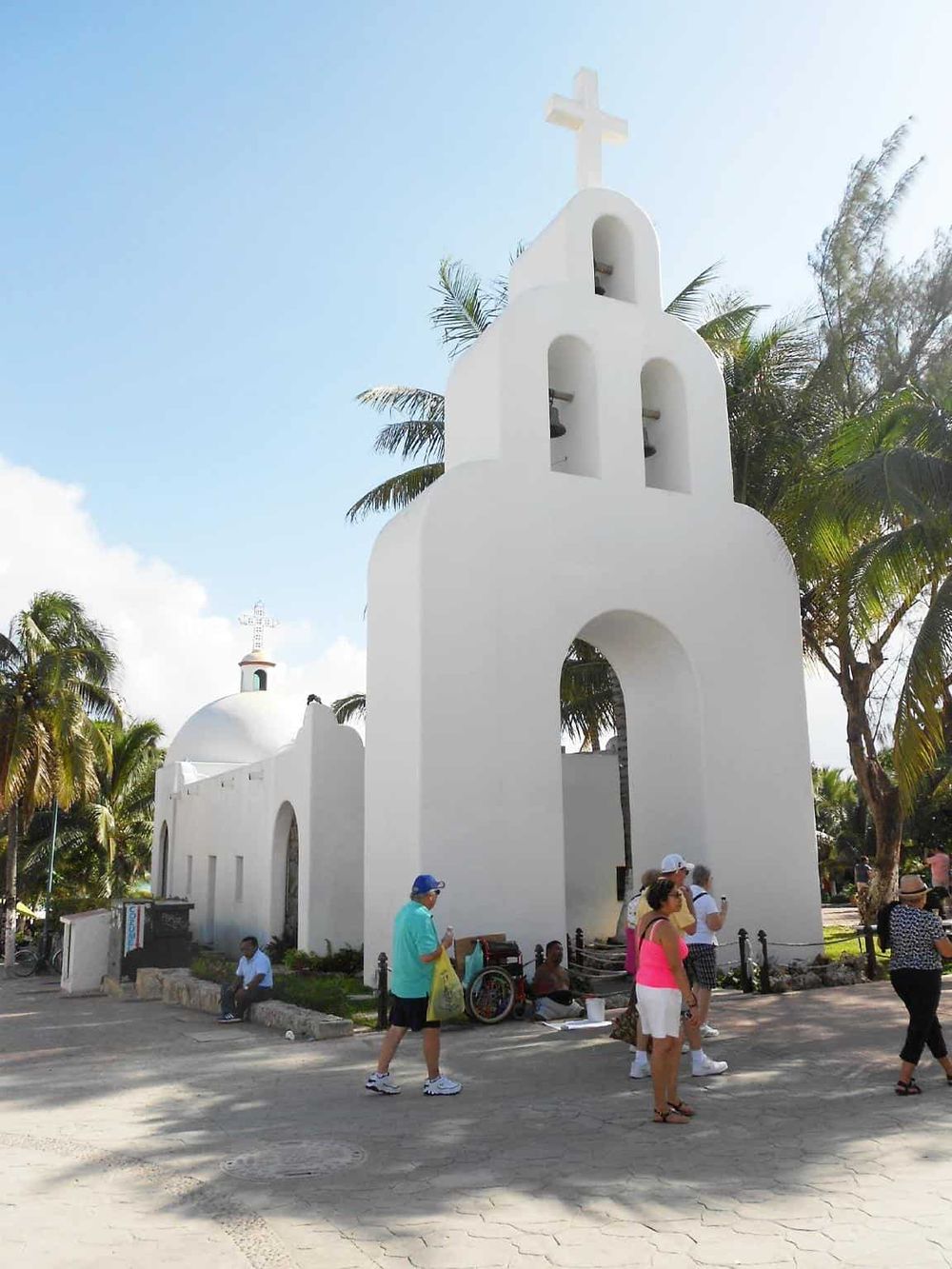Colorful church with white exterior, bell tower, and cross, surrounded by palm trees, popular tourist destination, vibrant atmosphere.