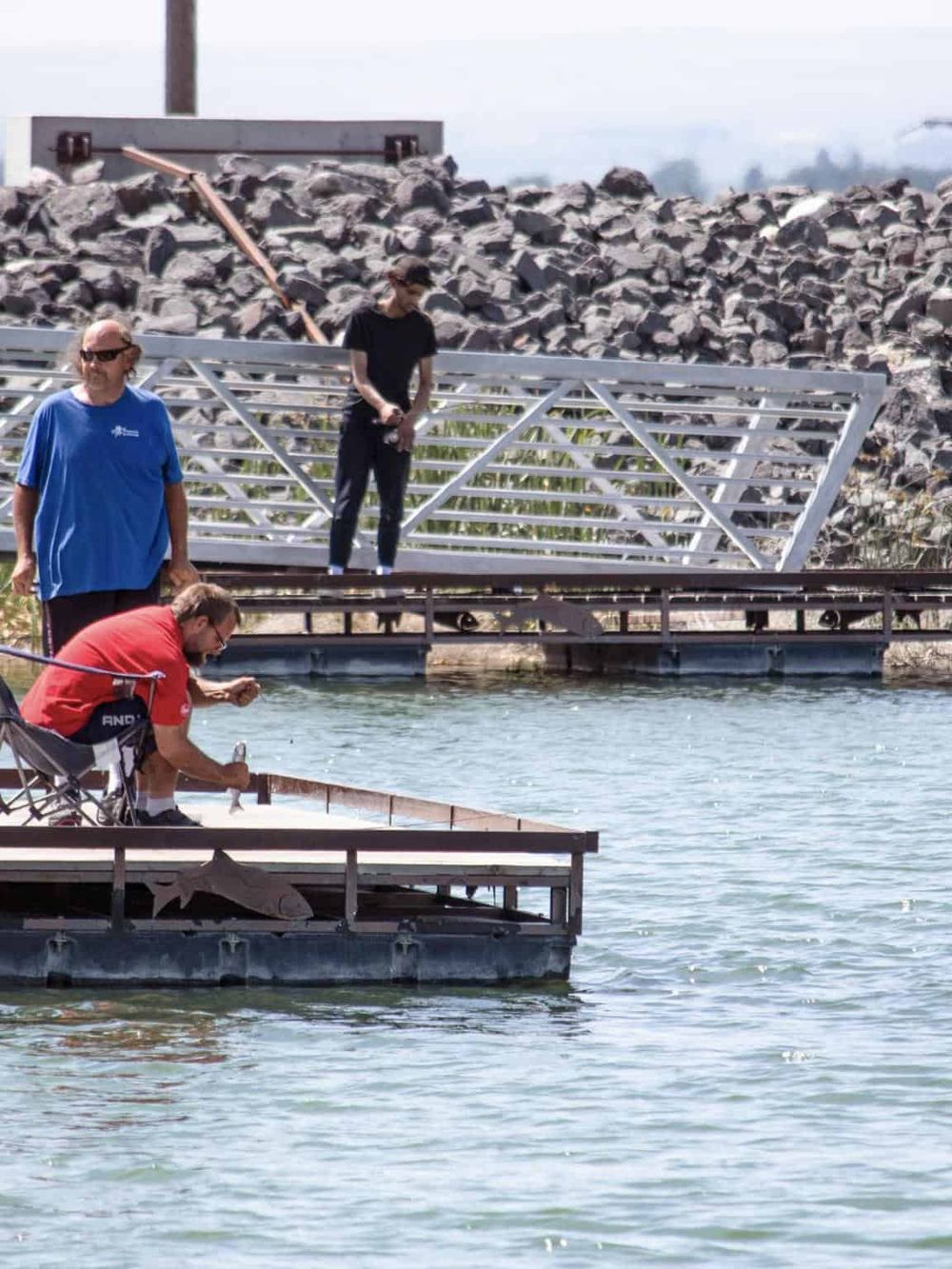 People fishing and relaxing at a dock by the water with a scenic background.