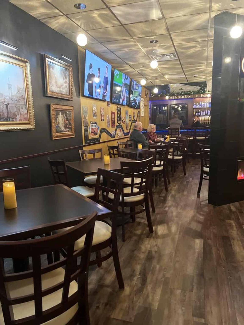 Cozy bar and restaurant interior with wall art, multiple TV screens, and dim ambient lighting.