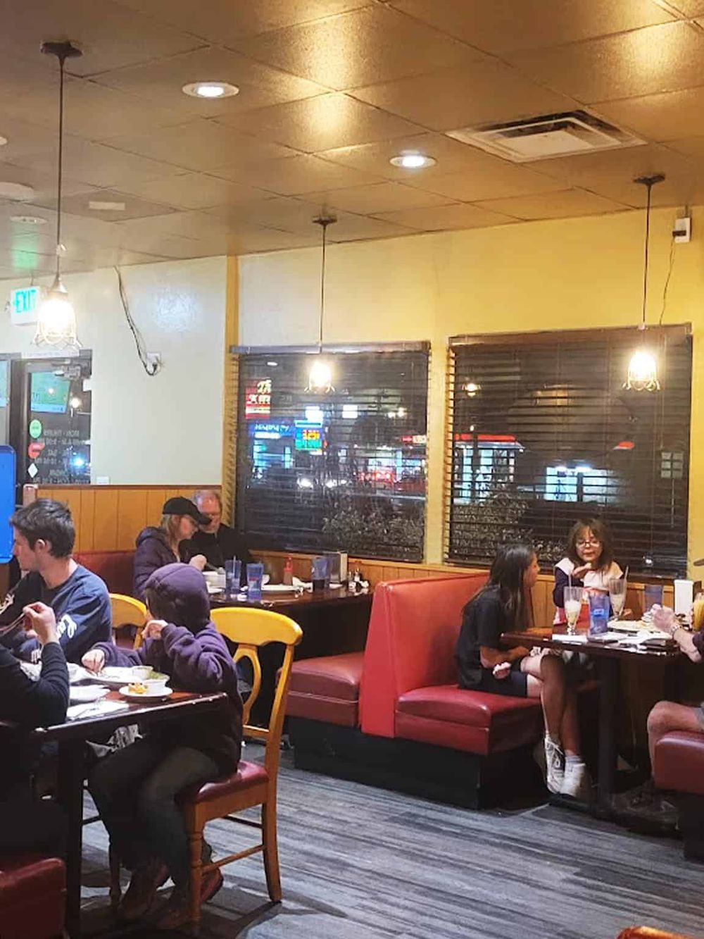 Cozy restaurant interior with groups of people dining, warm lighting, and large windows overlooking city nightlife.