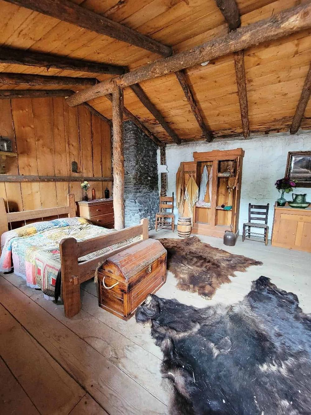 Cozy rustic bedroom with wooden furniture and animal hide rugs, perfect for a country getaway.