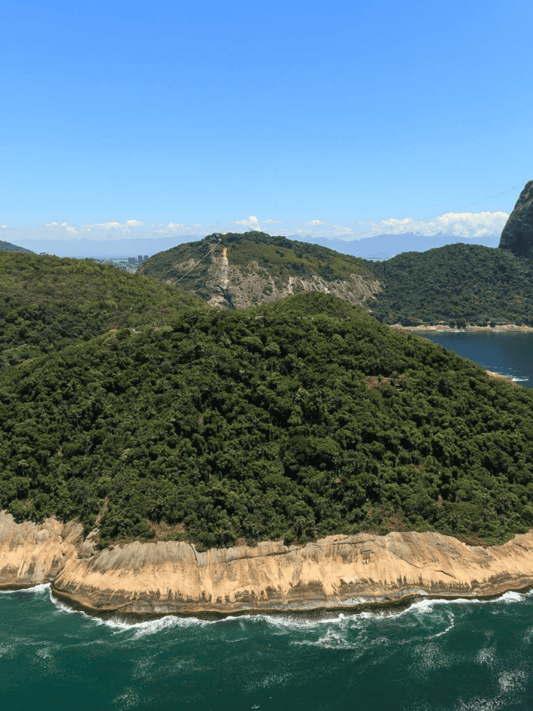 Lush green coastal mountain landscape with ocean waves crashing at the shore.