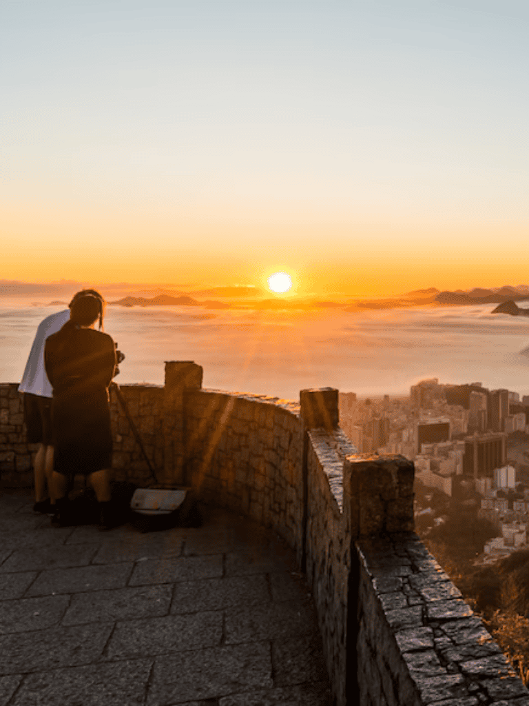 Breathtaking sunset view from a mountain lookout over a cityscape with two people taking photos.