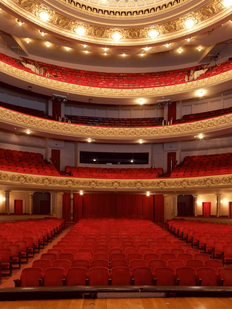 Ornate theater auditorium with plush red seats and decorative gold accents.
